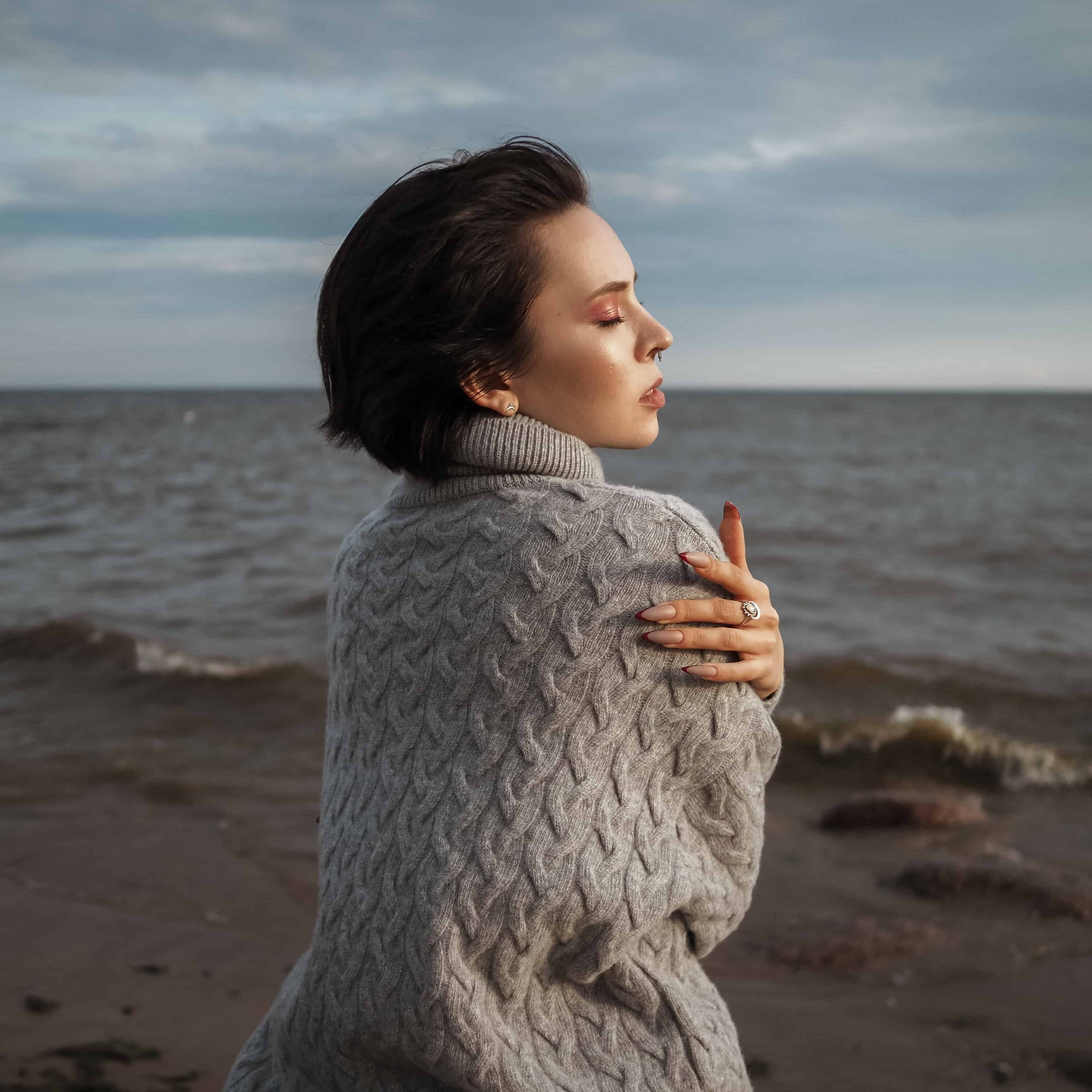 A woman sat on a rock at the beach self hugs