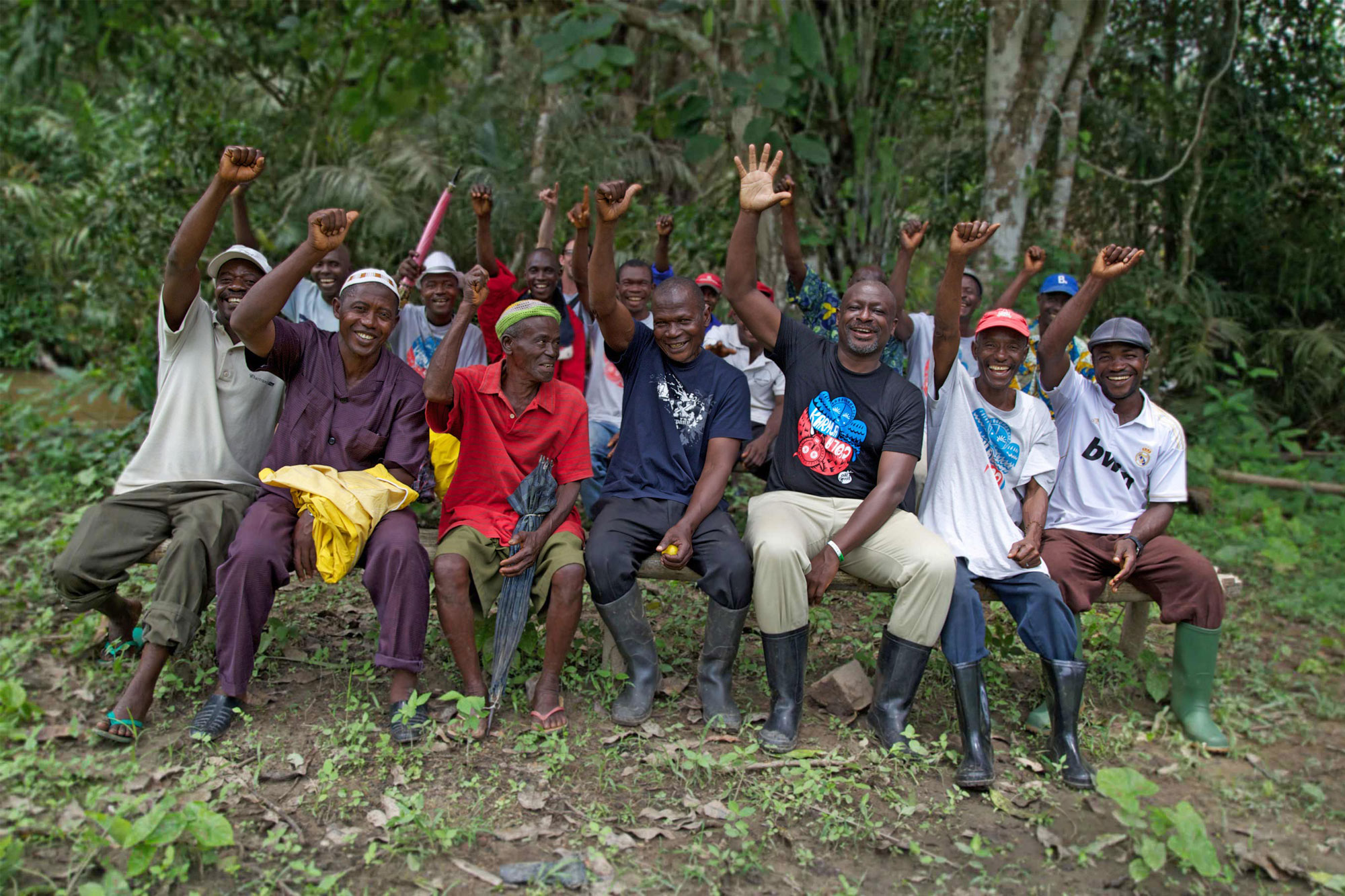 Albert, from the Karma Foundation, sitting with local farmers in Sierra Leone. The group are all smiling and waving to the camera