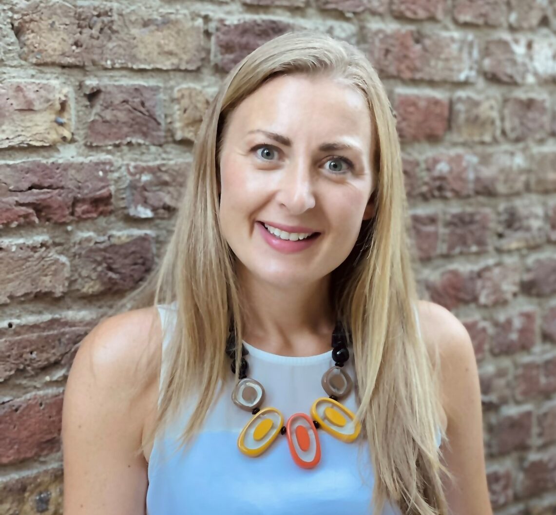 Photo of Laura Chambers standing against a brick wall smiling