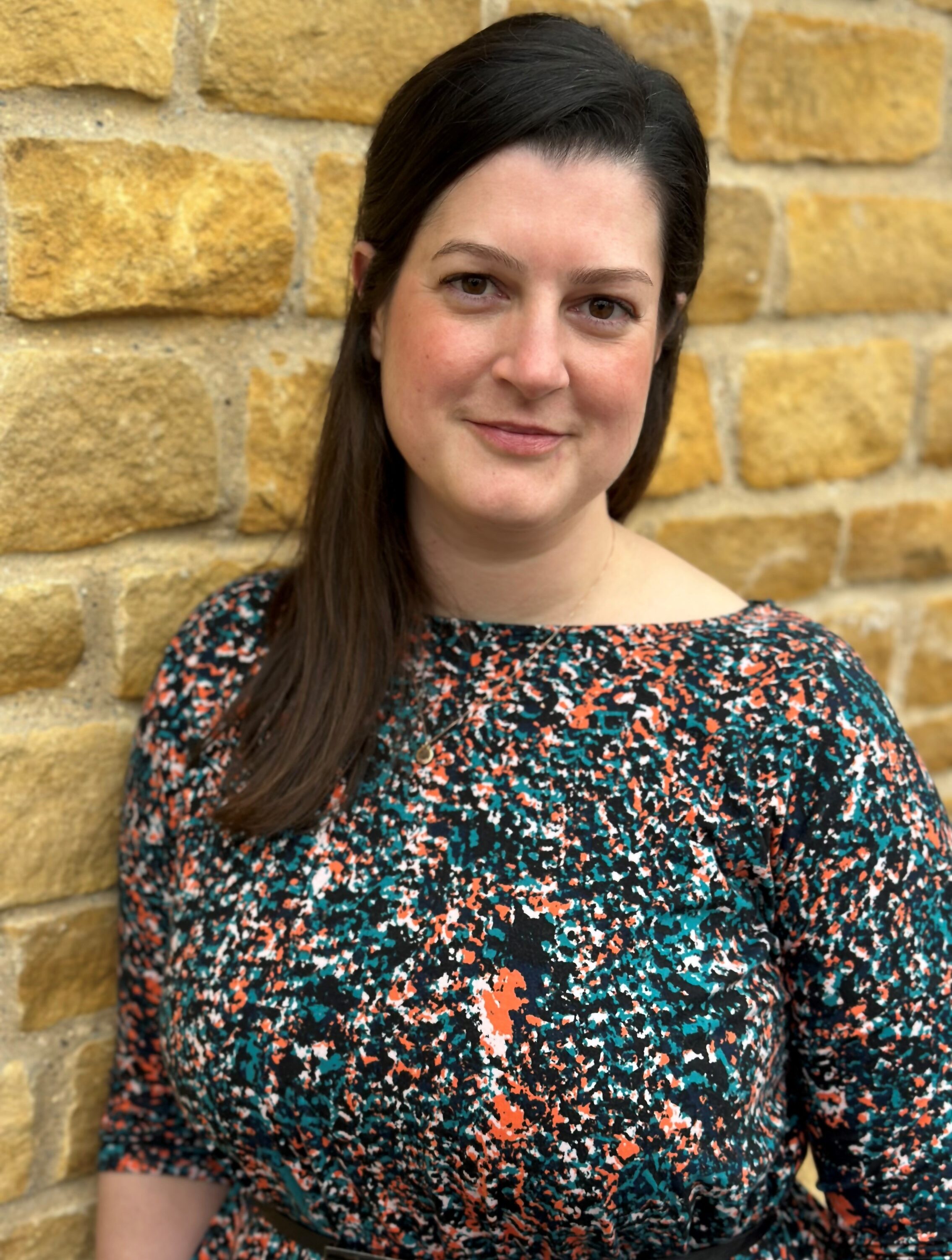 Photo of Nyree Ambarchian standing against a brick wall smiling