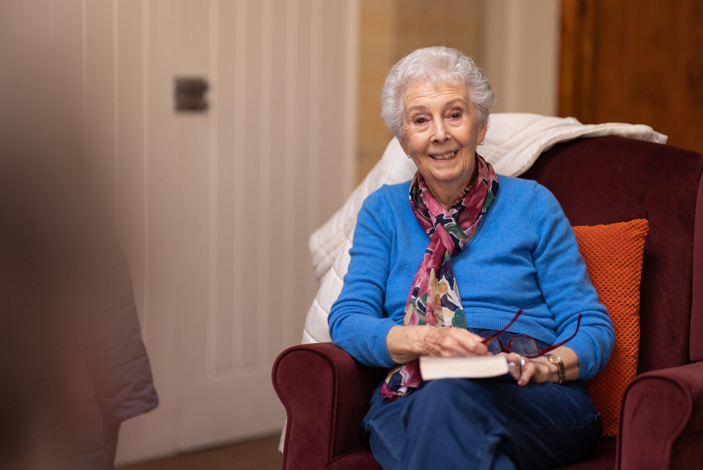 Photo of older woman sitting in chair holding a book and smiling