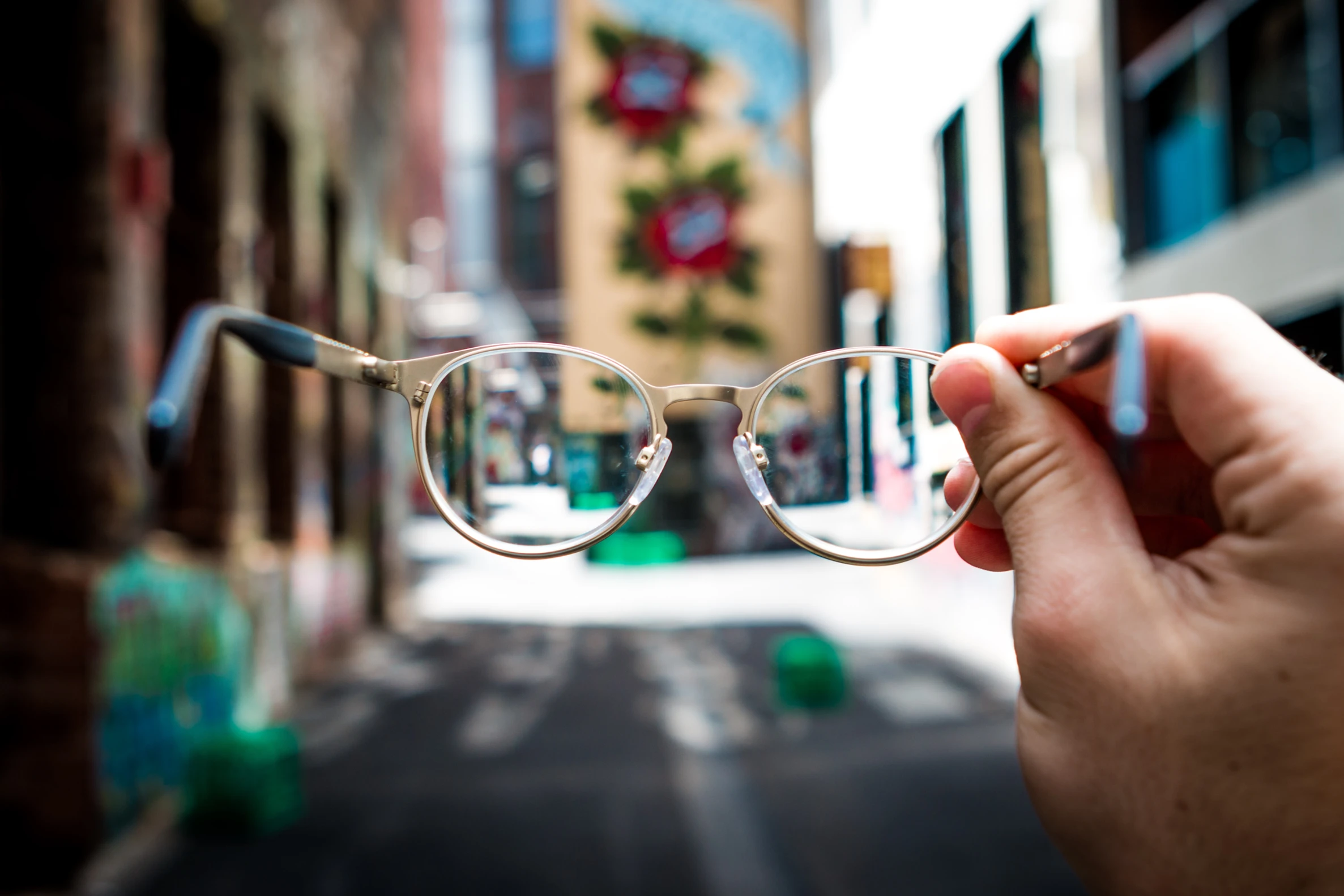 A pair of glasses are held up in front of the camera, making the unfocused street ahead clearer