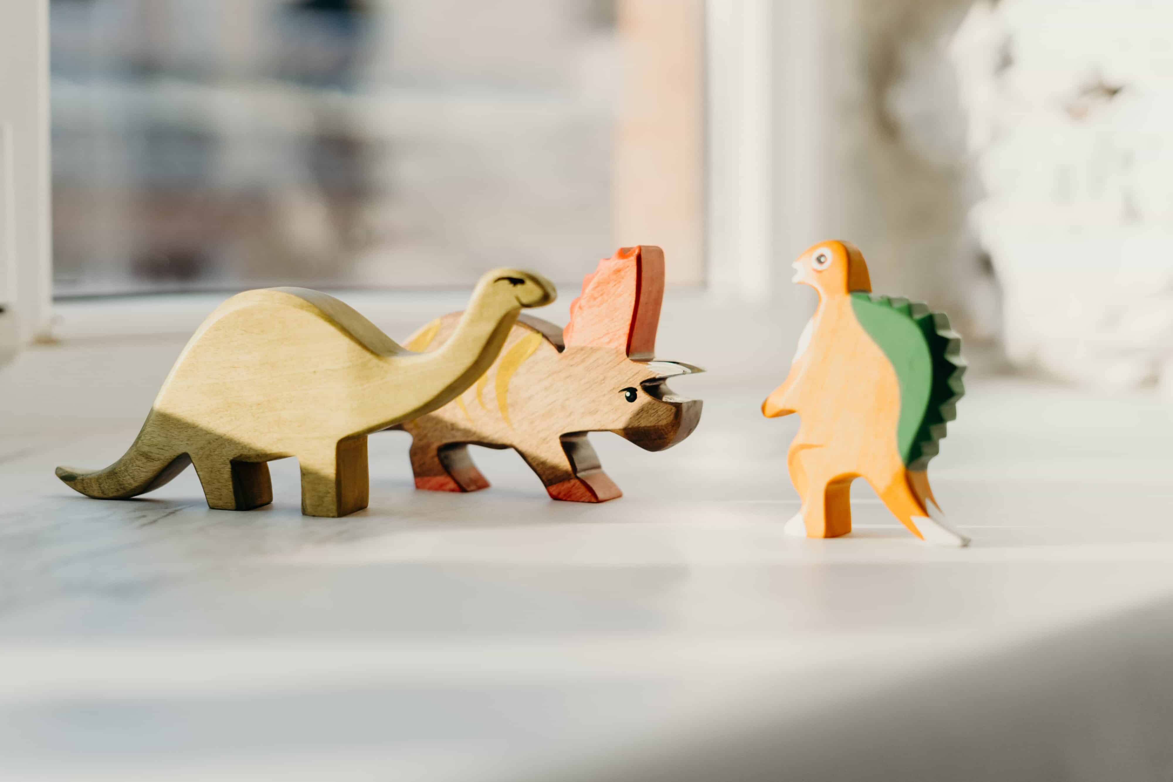 Wooden dinosaur figures face each other on a bright windowsil.